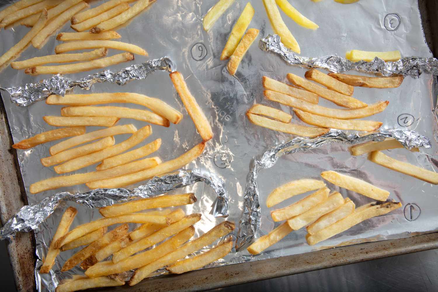 Various types of French fries arranged in sections on a foillined baking sheet