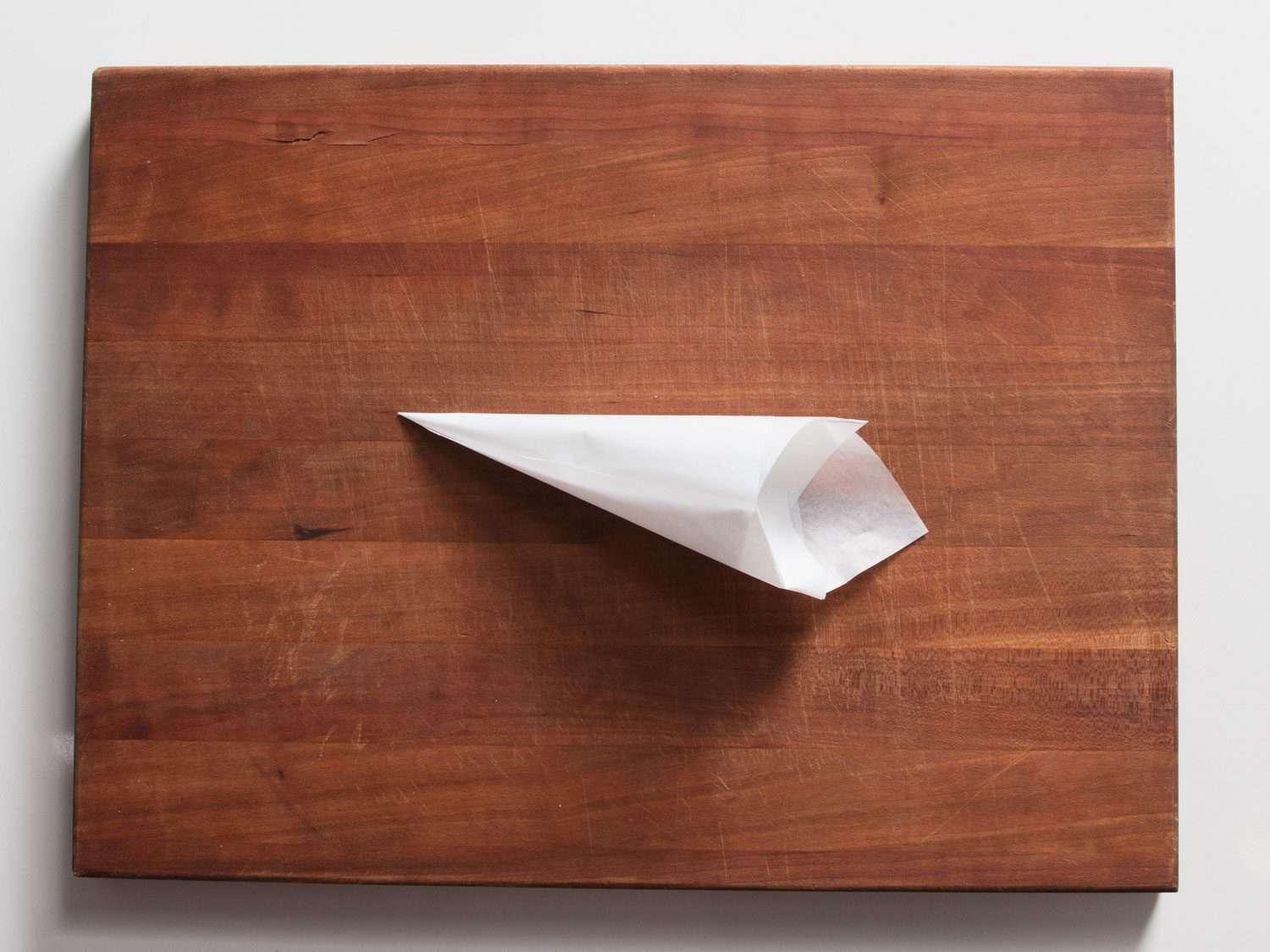 A parchment piping bag resting on a wooden cutting board.