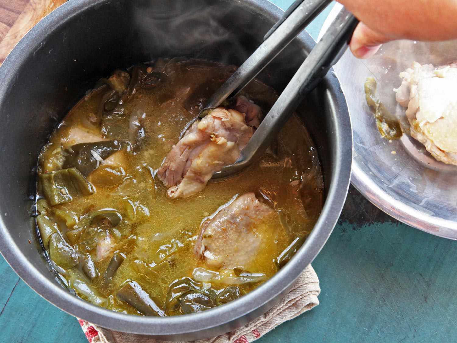 Using tongs to remove chicken thigh from pressure cooker filled with chicken green chili (chile verde).