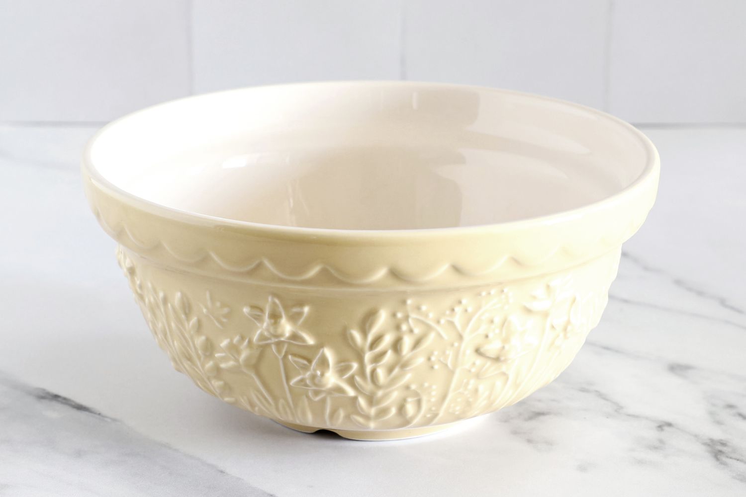 A Mason Cash bowl with embossed floral patterns and a scalloped rim placed on a light surface