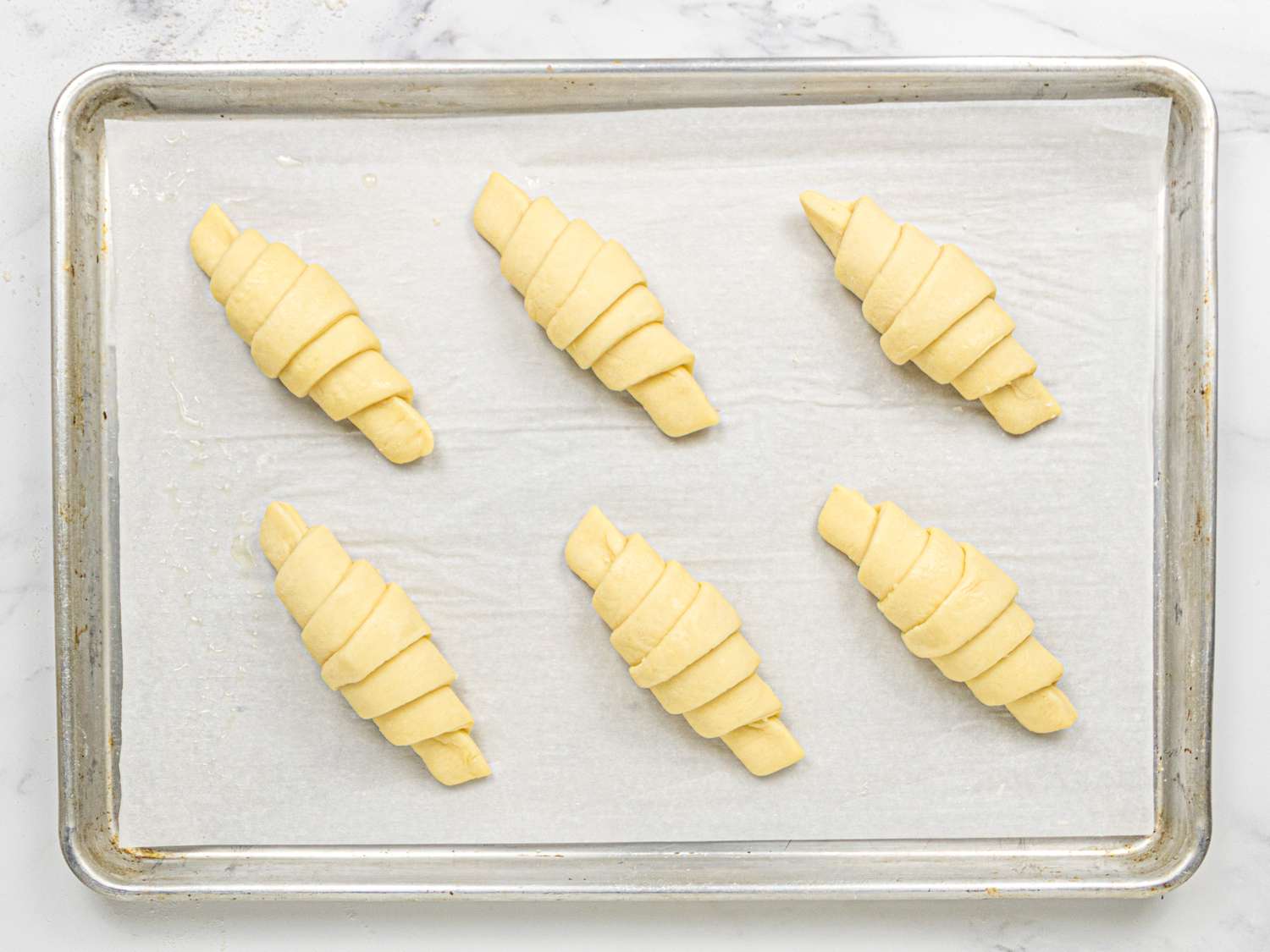 Six unbaked croissants arranged on a parchmentlined baking sheet