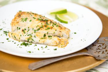 Broiled bluefish fillet garnished with chopped parsley and lime slices on a plate