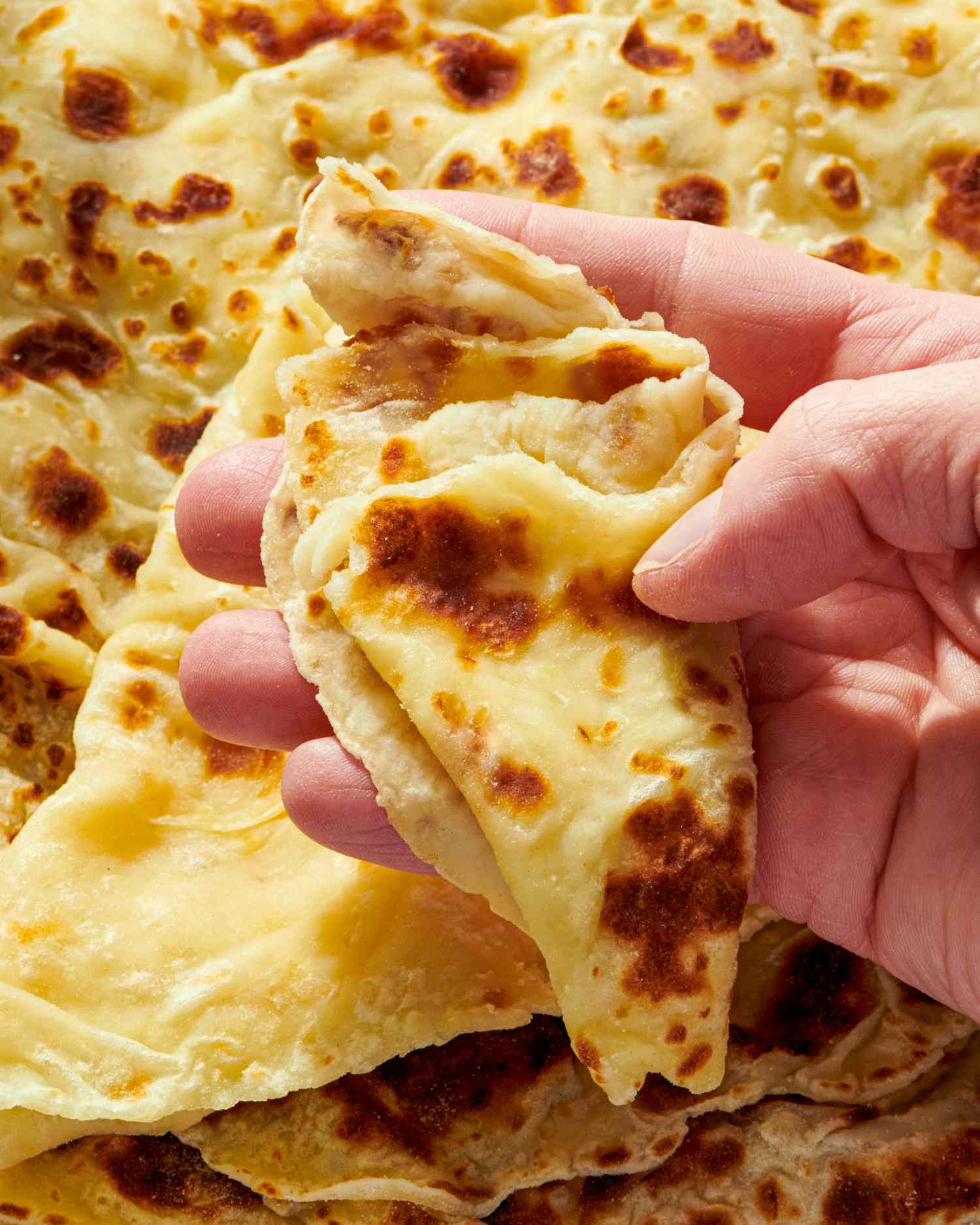 A hand holding a folded lefse flatbread
