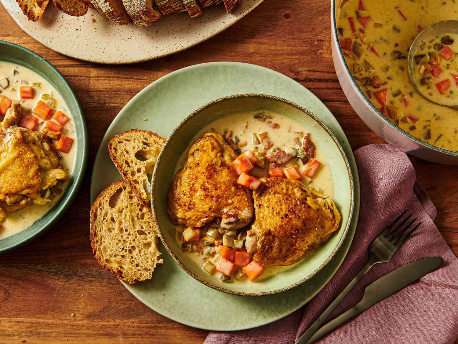 A plate of chicken served with vegetables and bread next to a bowl of soup