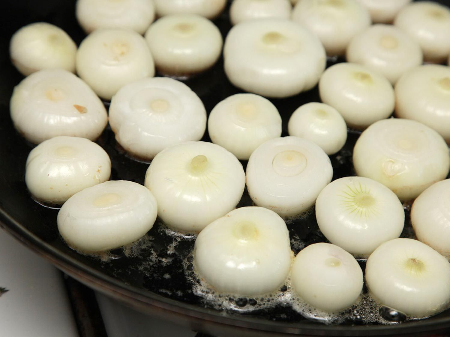 Peeled cipollini onions in a cast iron skillet, at the beginning of the caramelization process.