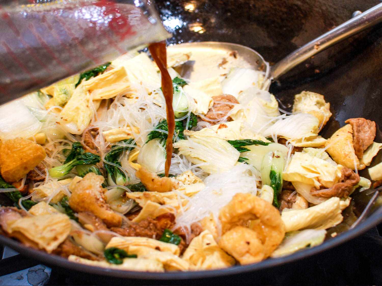 Pouring sauce over the Buddha's Delight in a wok.