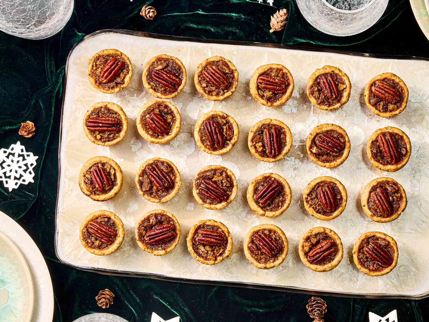 Decorative board with pecan tassies on it, on top of a dark green velvet fabric. 2 cups of water.
