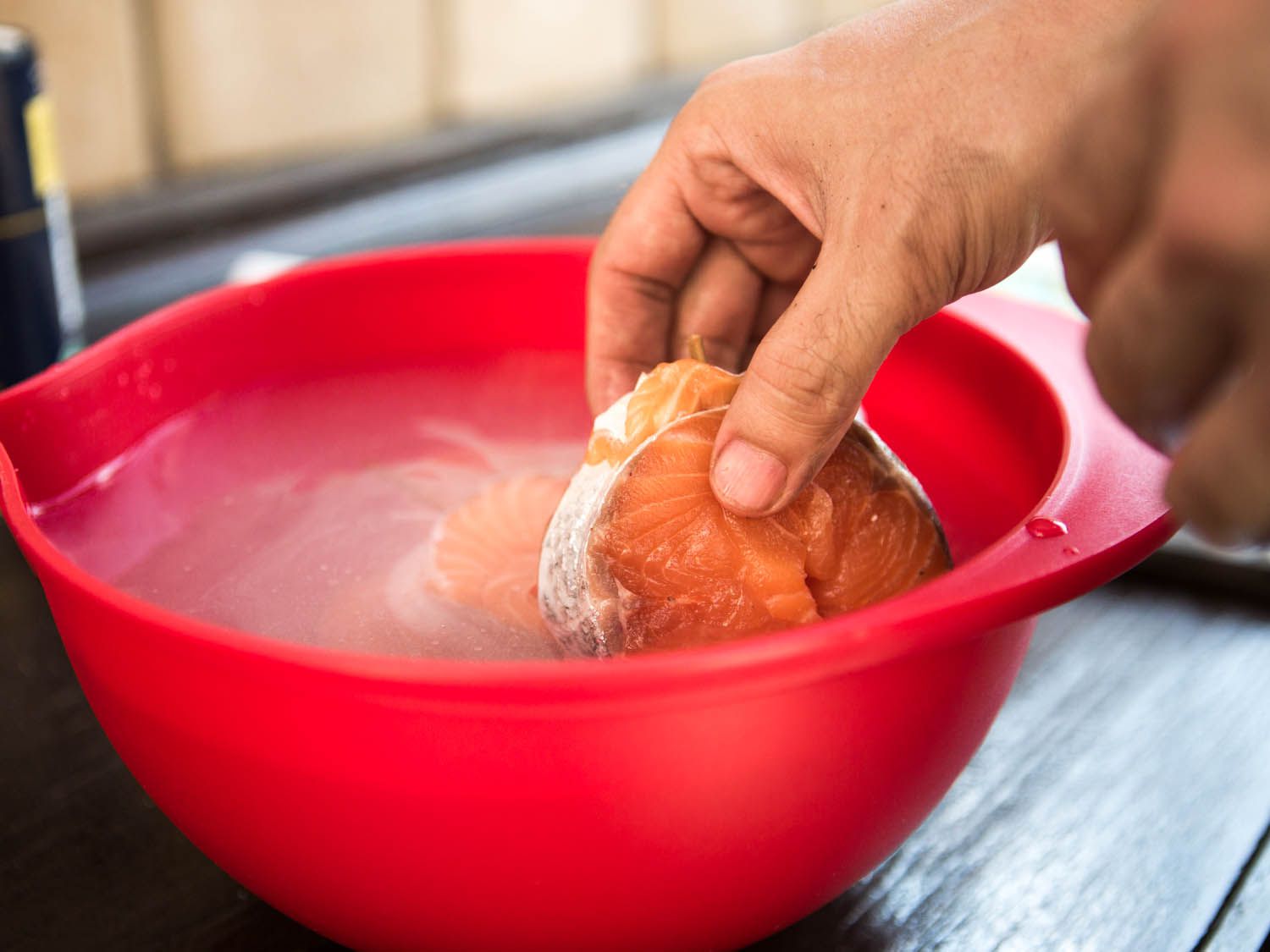 Placing tied salmon steaks in a red bowl of brine.