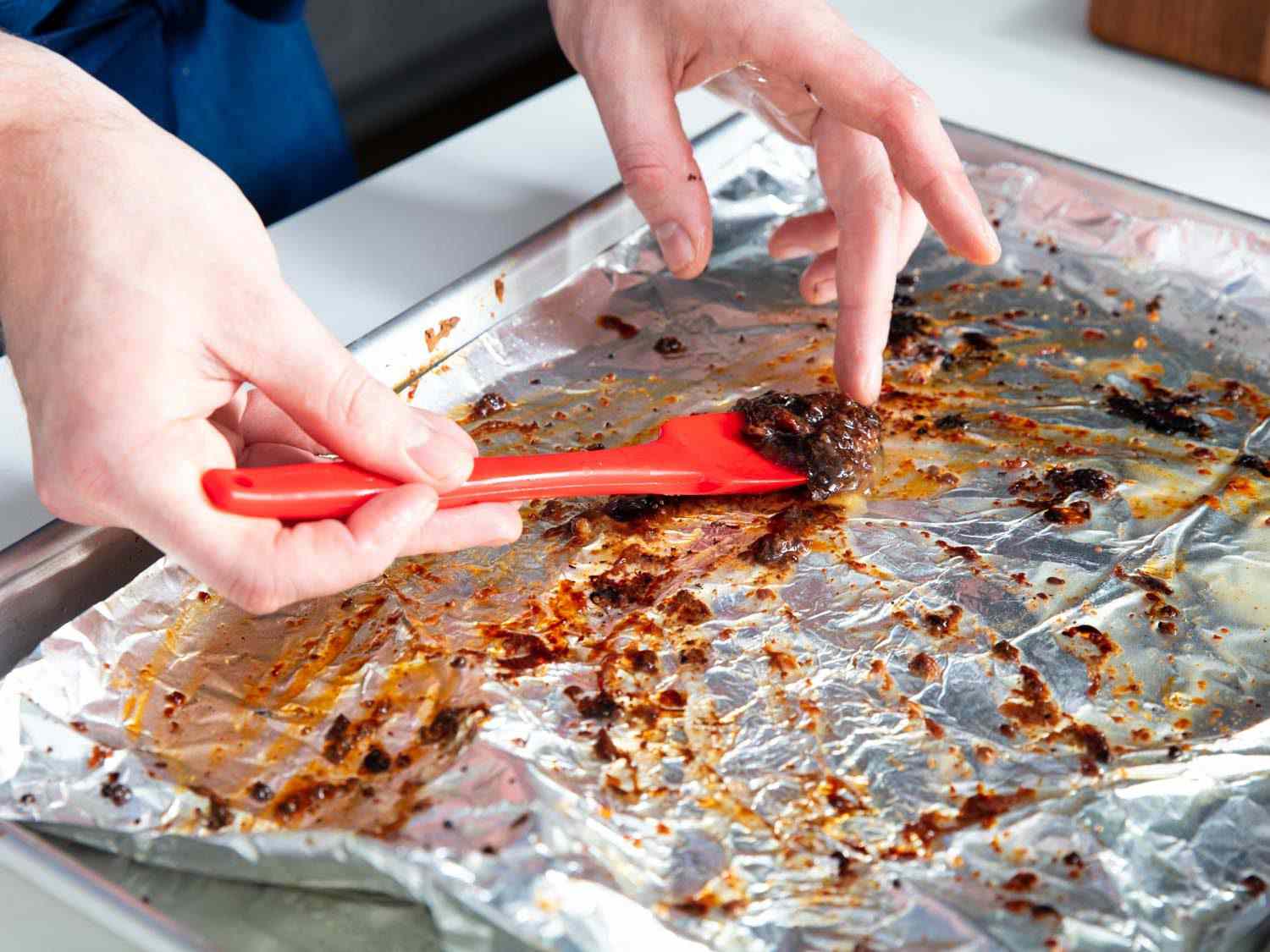 Scooping up prime rib drippings from a foil-lined baking sheet.
