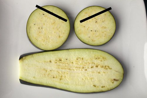 A long slice of eggplant is positioned below to cross-cut slices to form a frowny face.