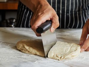 A person uses a bench scraper to cut a large piece of dough