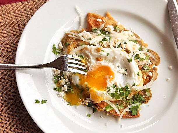 Overhead shot of fork breaking into runny yolk of sunnyside egg on chilaquiles.