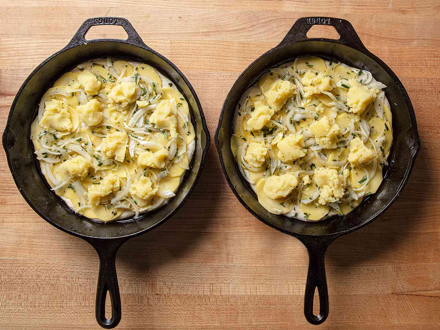 Two cast iron pans side by side containing the prepped but unbaked pizzas.