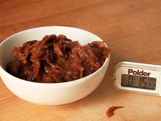 A bowl of dark brown caramelized onions next to a timer set to 15 minutes.