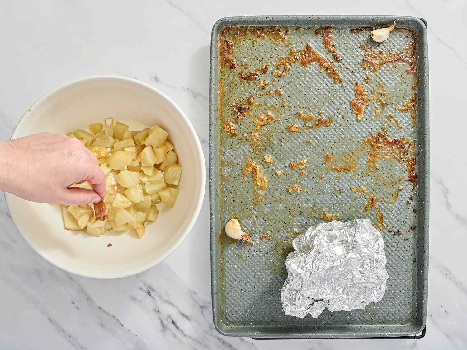 Roasted garlic cloves being removed from a baking sheet with foil and placed in a bowl