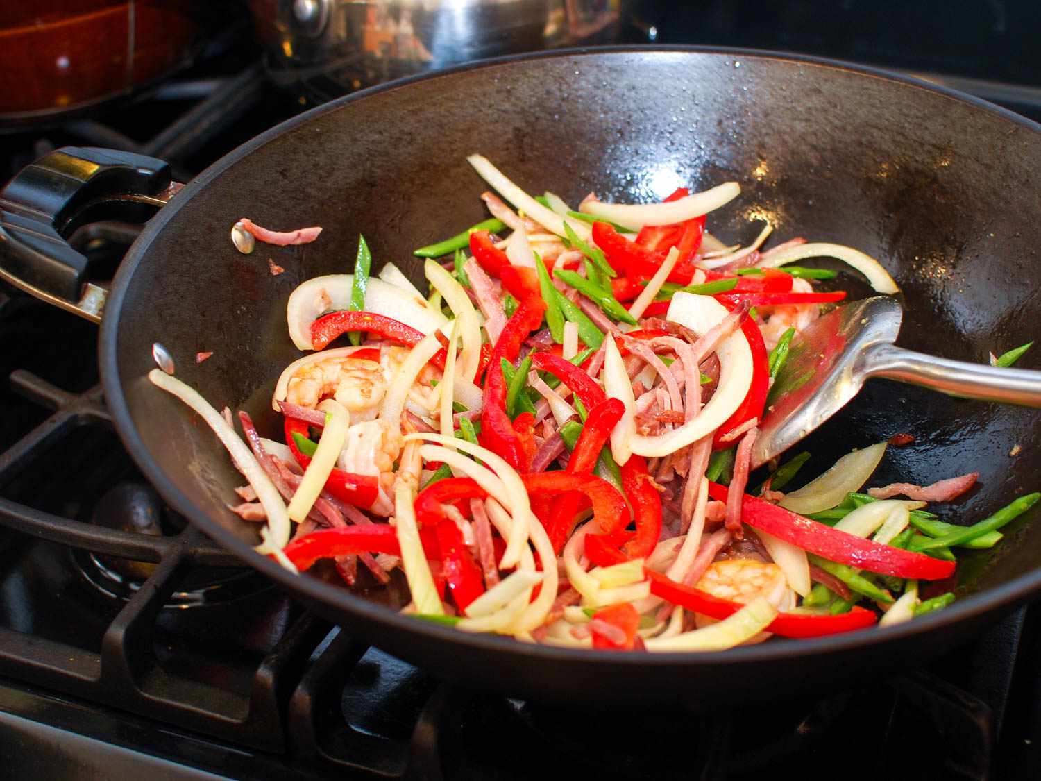 Spatula stirring curry powder into shrimp, char siu, and vegetables in a hot wok.