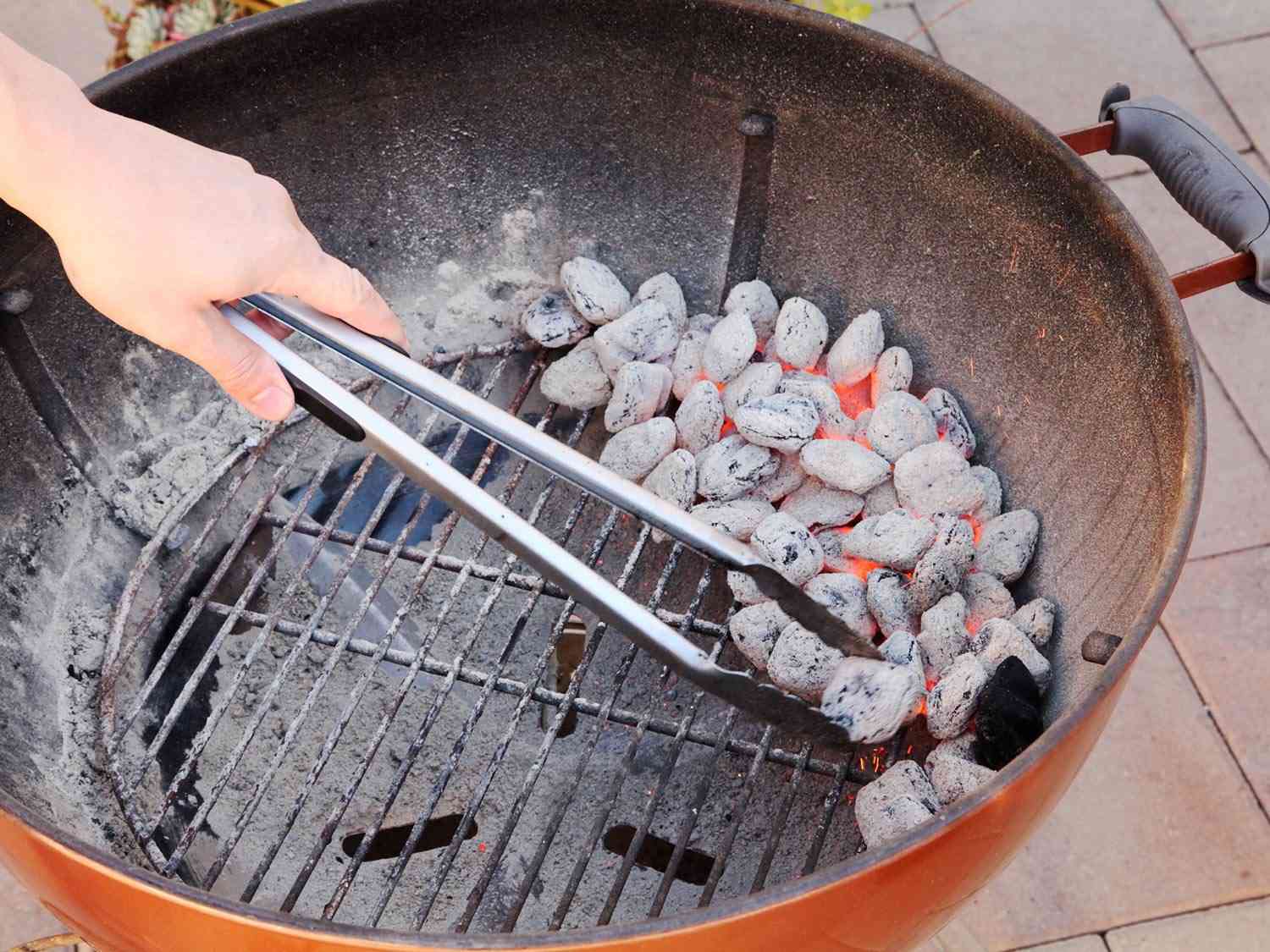 Arranging lit coals on one side of a grill grate for a two-zone fire.
