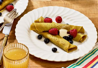 ployes with butter and berries on white dishes, with a fork and knife, striped napkin, and a wooden tabletop