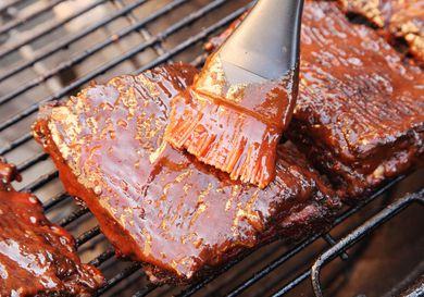 Brushing barbecue sauce on top of ribs on the grill