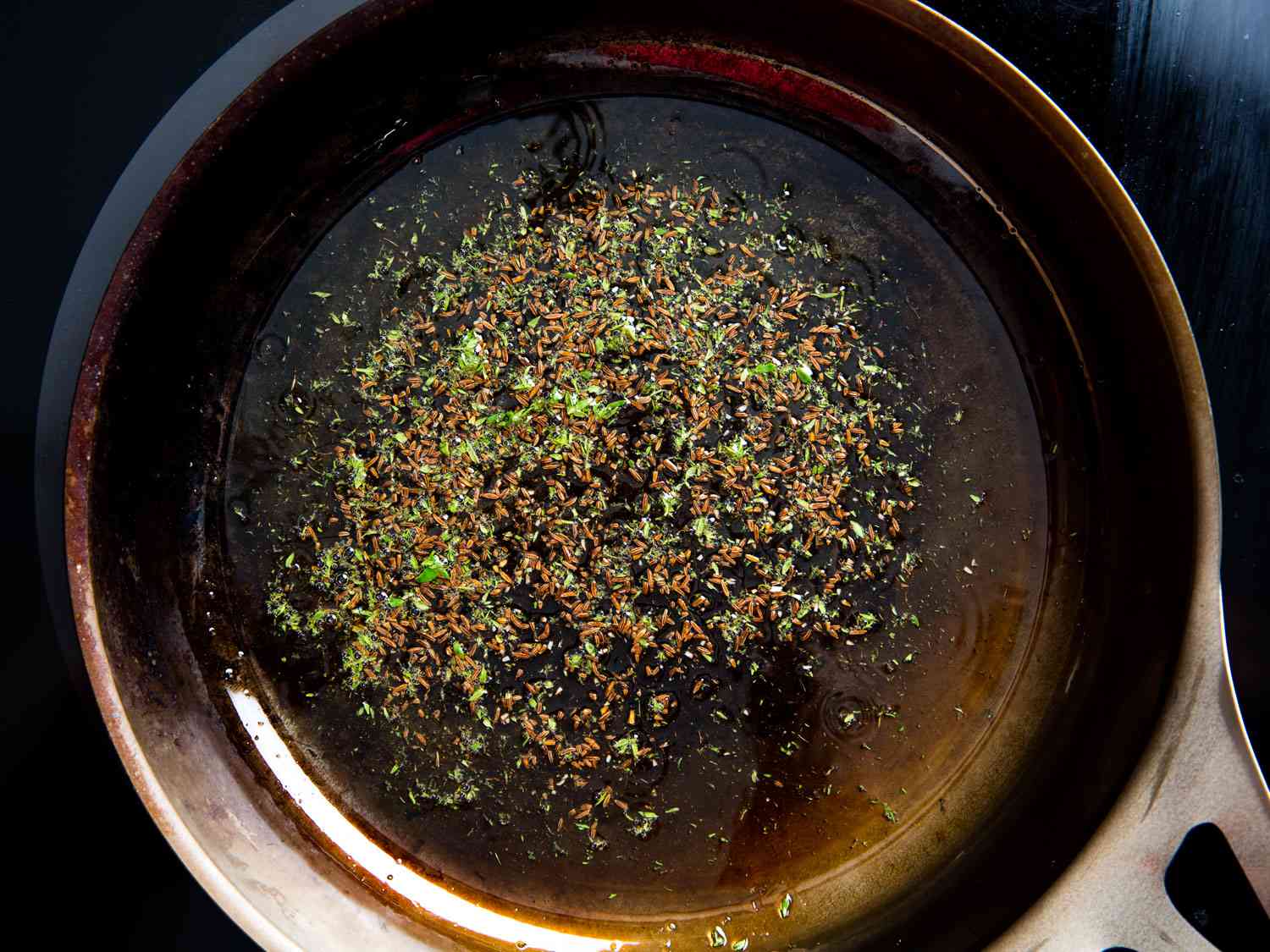 Caraway and thyme frying in oil in a carbon steel skillet.