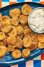 Blue platter with fried pickle and a small bowl of dip, with a hand dipping one pickle 