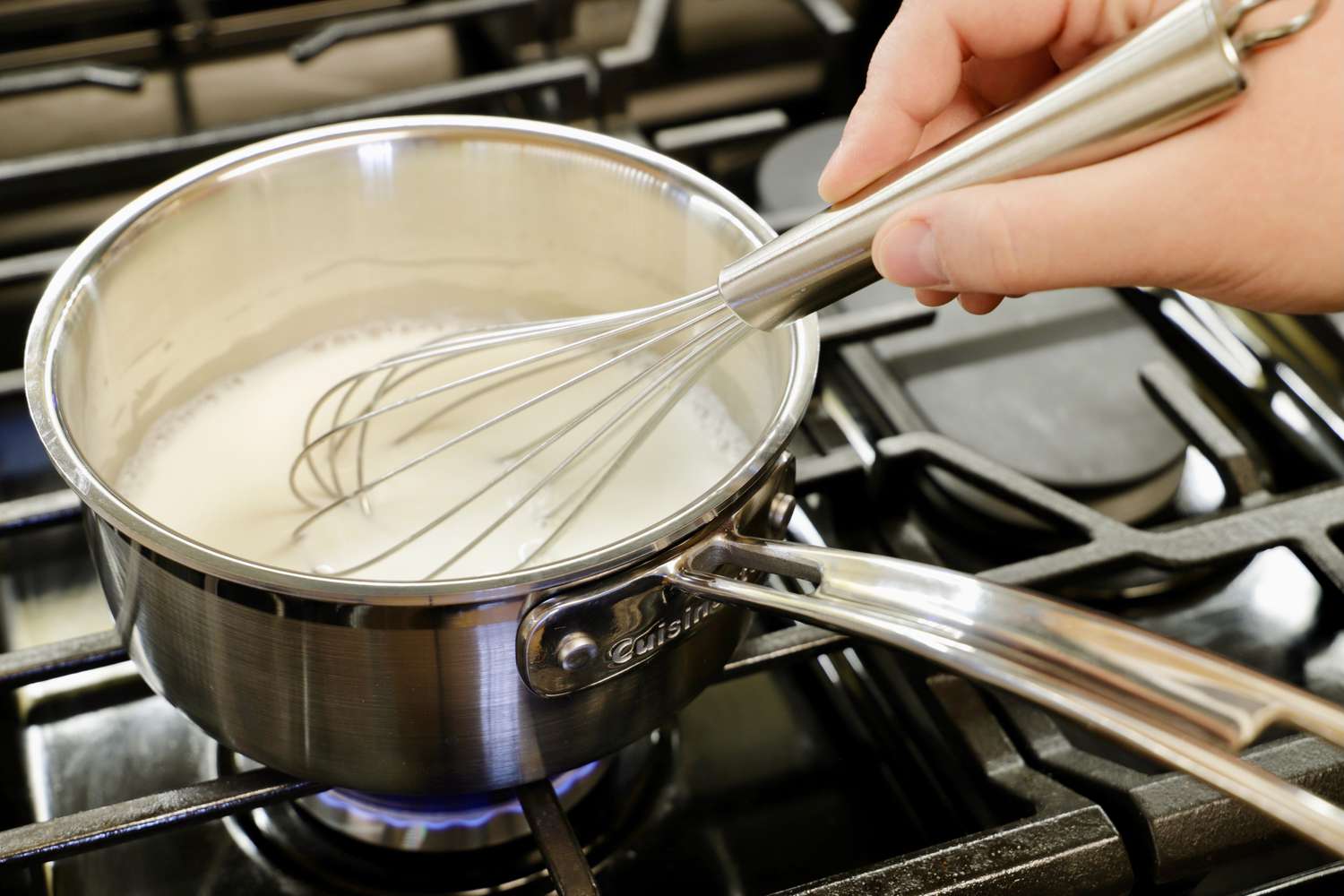 a person whisking milk in a small saucepan