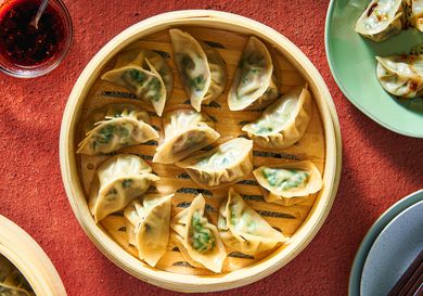 A wooden steamer basket holding steamed, translucent pork and chive dumplings.