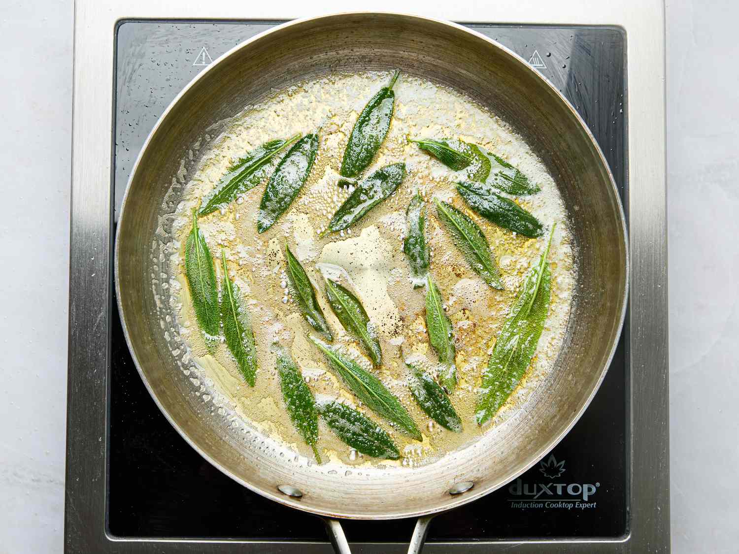 Sage leaves frying in butter in a skillet on an induction cooktop