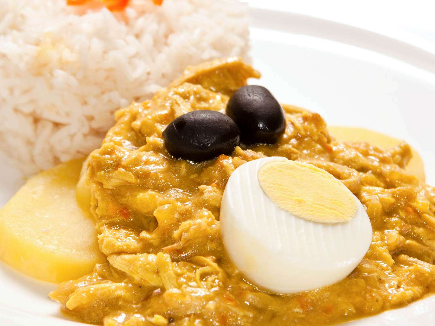 A plate of Peruvian aji de gallina with rice, potato, black olives, and a boiled egg half.