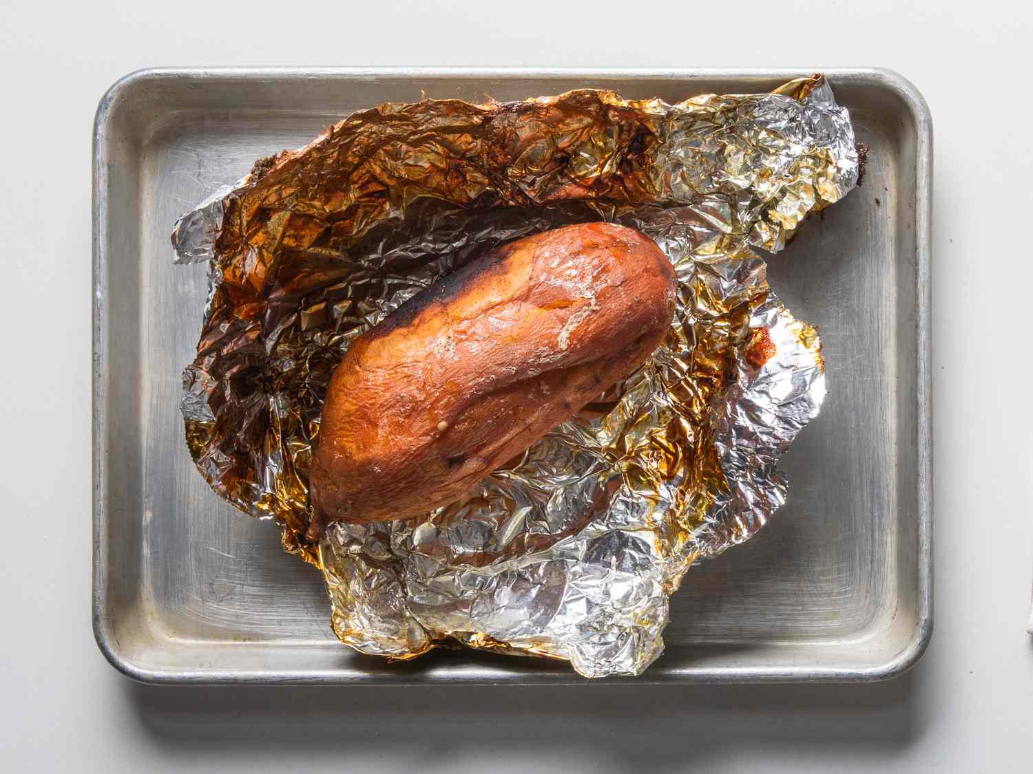 Frozen roasted sweet potato with foil wrap unwrapped on a rimmed baking sheet