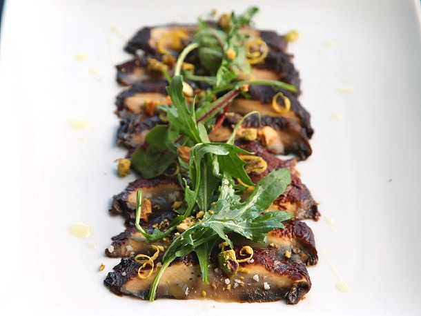 Closeup of the finished mushroom carpaccio, topped with lemon zest, chopped pistachio, and arugula.