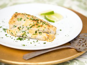 Broiled bluefish fillet garnished with chopped parsley and lime slices on a plate