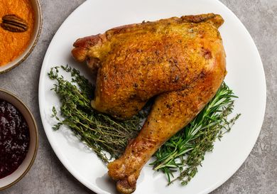 A sous vide turkey leg on a bed of herbs next to sweet potatoes and cranberry sauce.