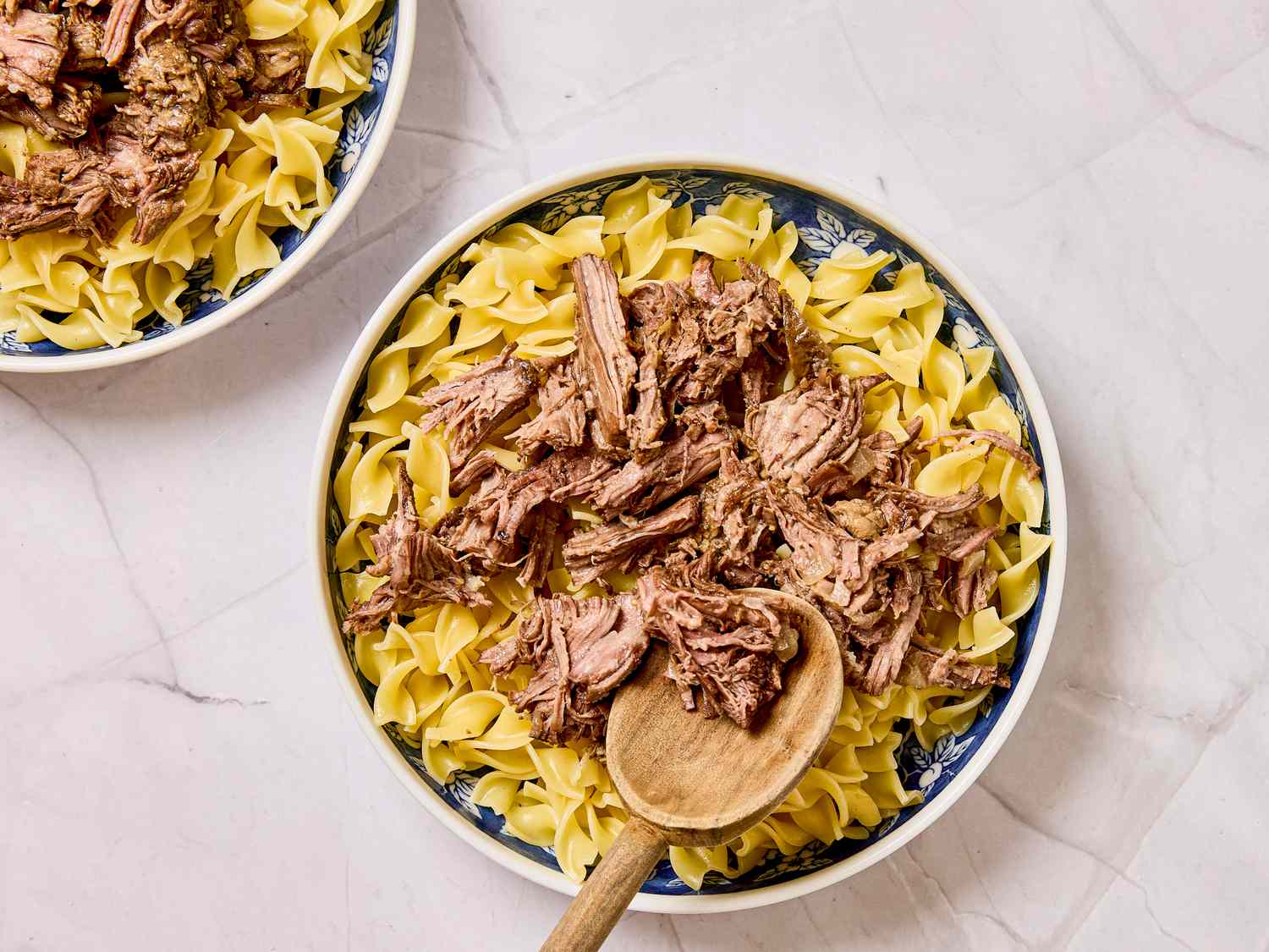 A bowl of beef stroganoff served over noodles with a wooden spoon