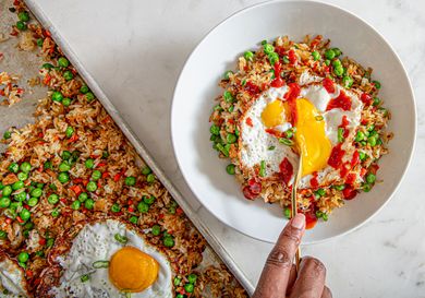 A serving of fried rice with peas and a fried egg on top, being scooped with a spoon from a white bowl