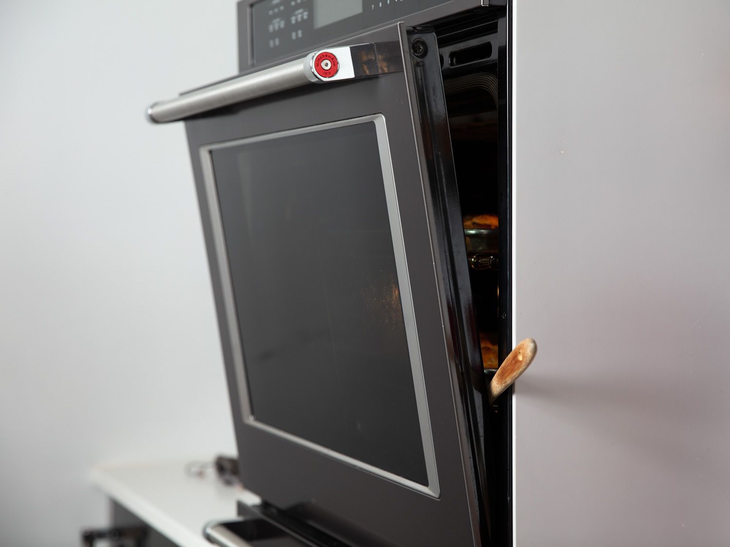 An oven with the door propped open with a wooden spoon.