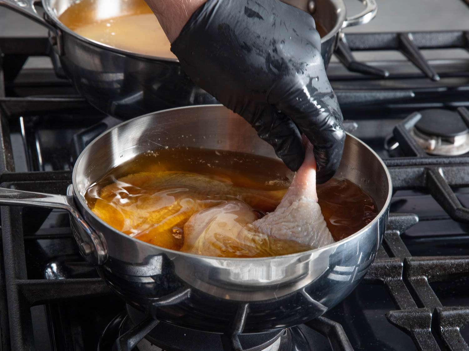 The marinated duck legs are added to a small saucepan along with rendered duck fat to cover.
