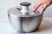 a person pressing the stop button on the oxo steel salad spinner