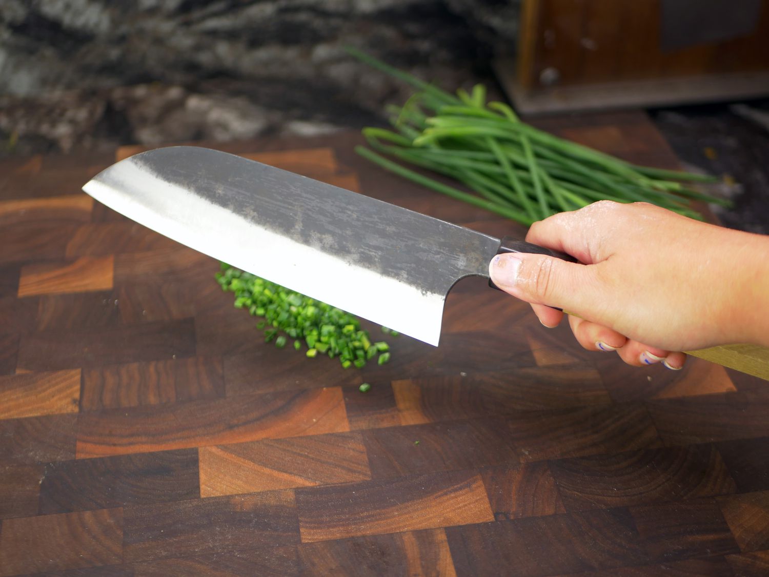 a person holding the sakai kikumori over a cutting board with minced chives