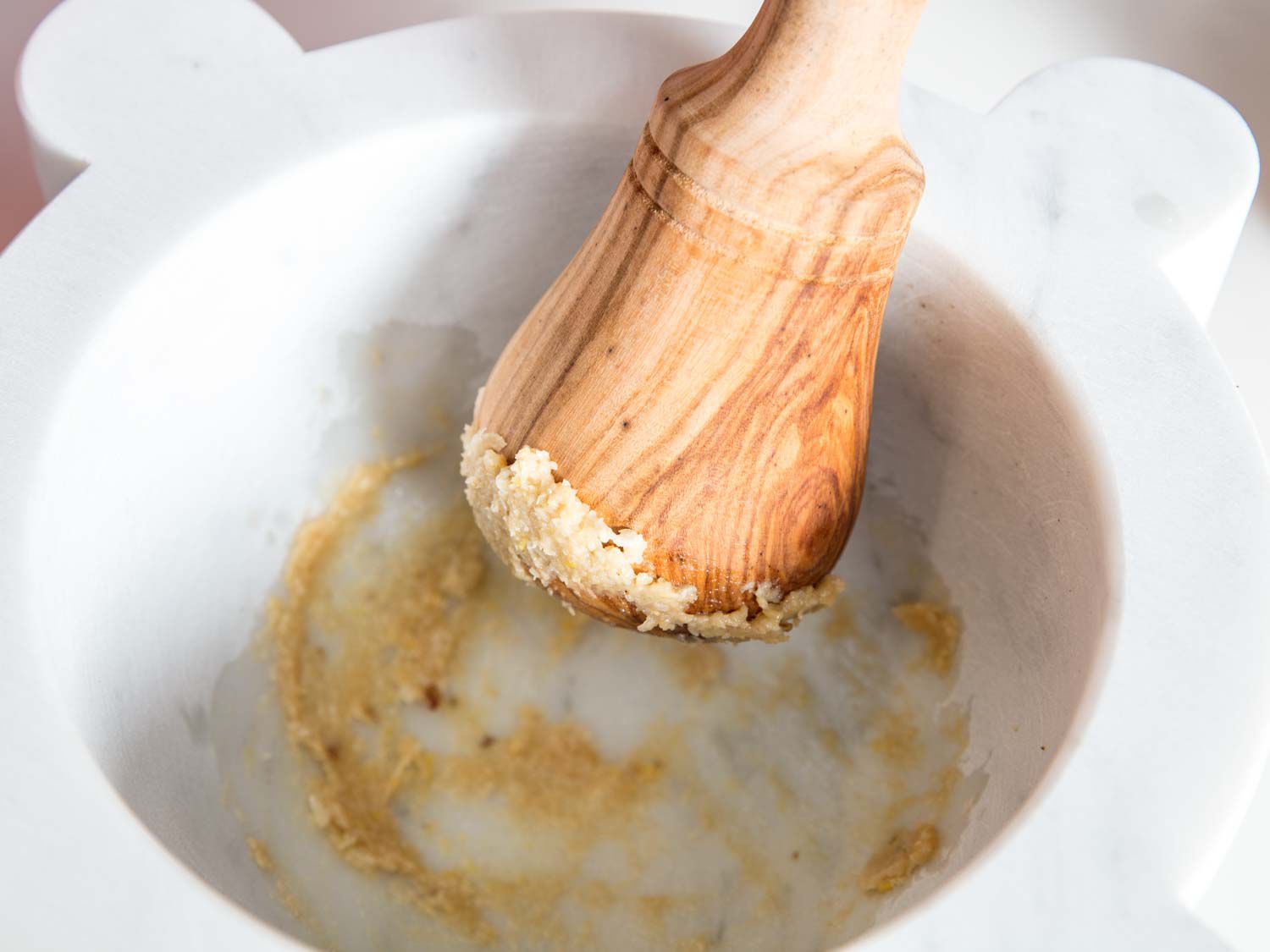 Pounding garlic to a paste using a marble mortar and wooden pestle.