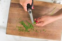 Herb scissors cutting chives on a wooden cutting board