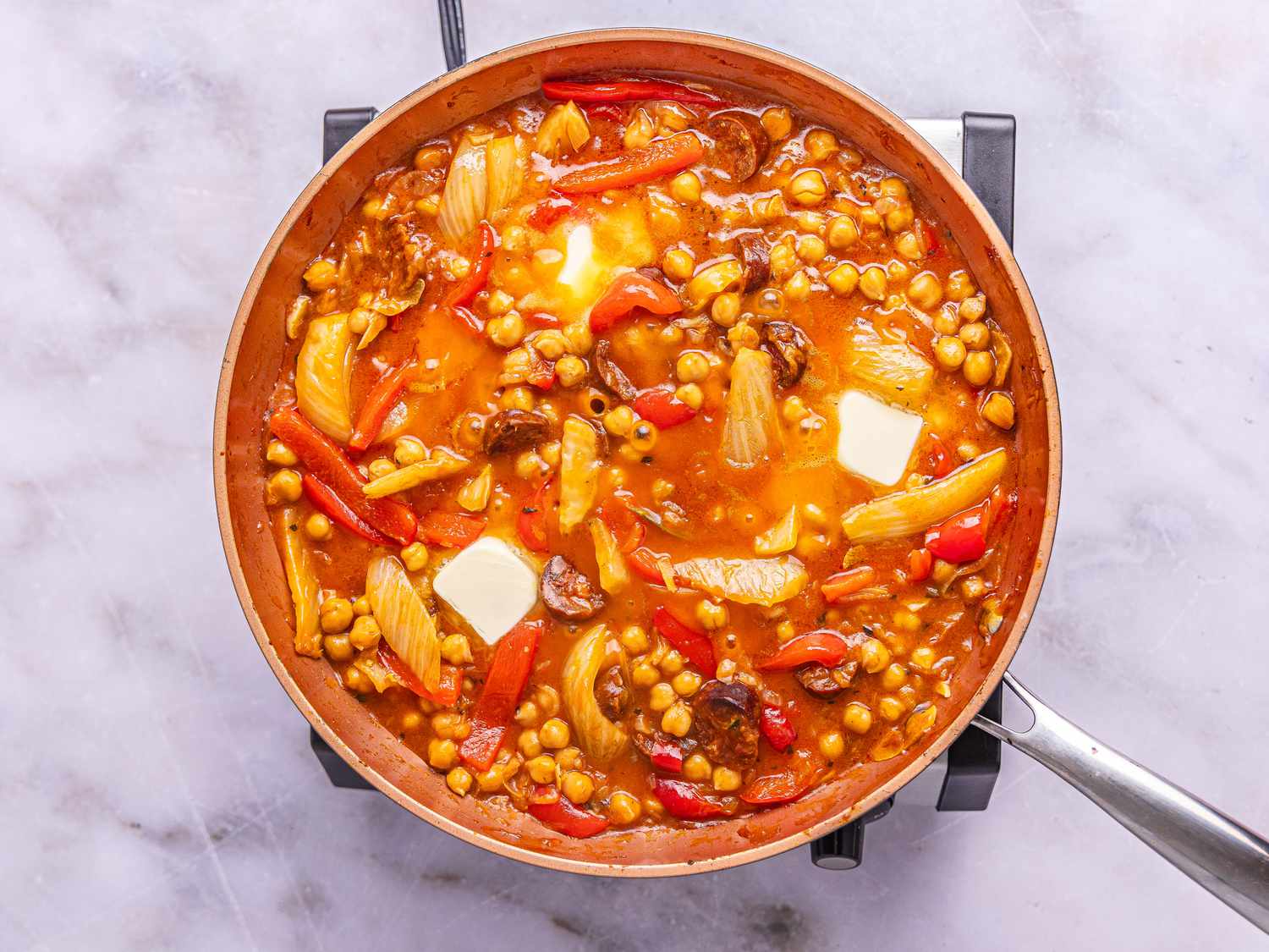 A pan containing a dish with chickpeas, peppers, onions, and visible butter