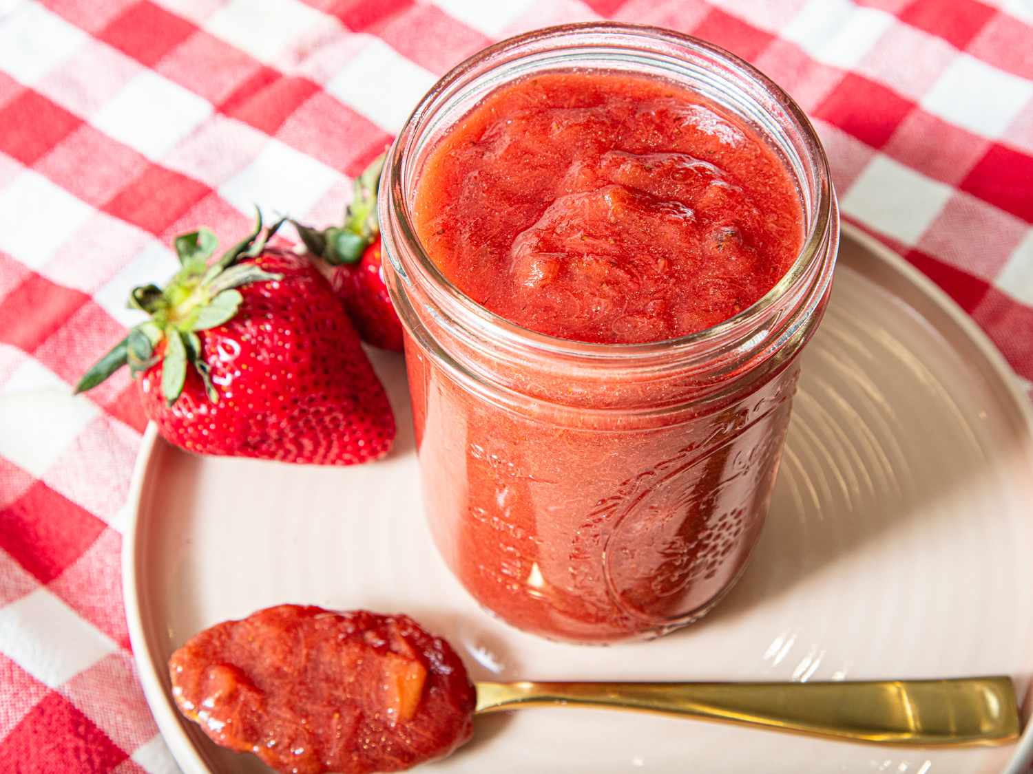 Jar of strawberry rhubarb jam with fresh strawberries on a plate