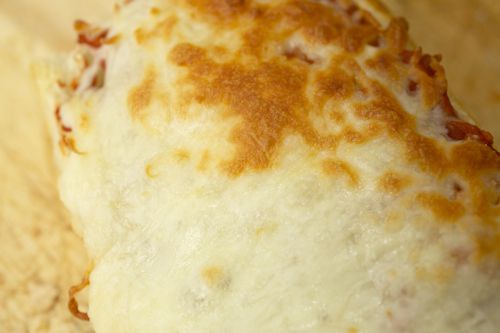 Closeup of melted pre-shredded mozzarella, which has developed a lightly browned crust during baking.