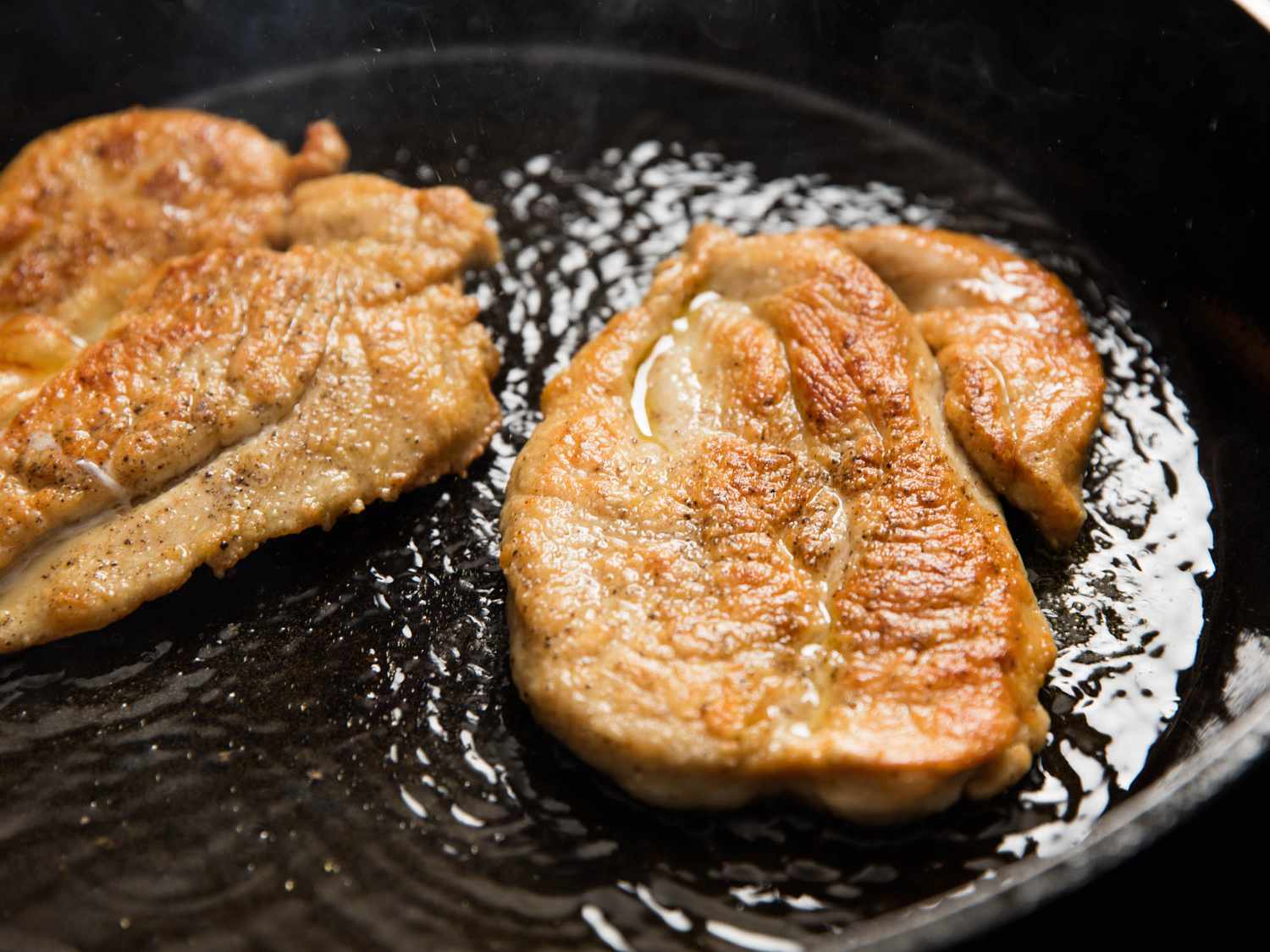 Chicken cutlets cooking in a skillet for chicken marsala.