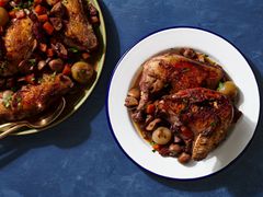 A white, blue-rimmed plate holding a large serving of Coq au Vin. On the lefthand side of the image is a round platter holding more of the Coq au Vin.