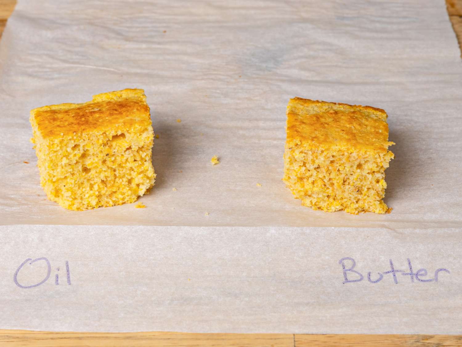 Two pieces of cornbread on parchment paper labeled as Oil and Butter underneath each piece