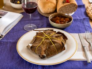 A wrapped dish on a plate bread and bowl of food in the background on a table
