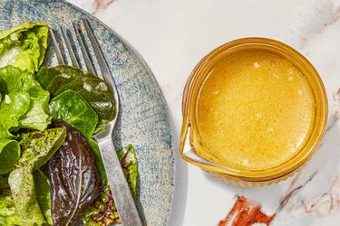 Lemon vinaigrette in a small bowl next to a plate of greens.