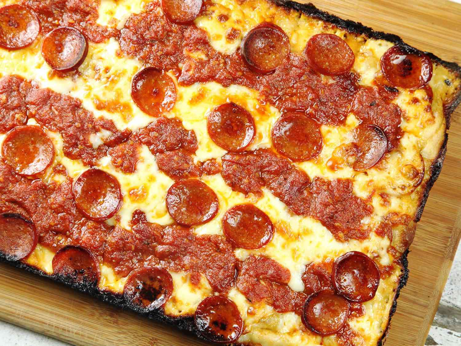 A slab of Detroit-style pepperoni pizza on a wooden cutting board.